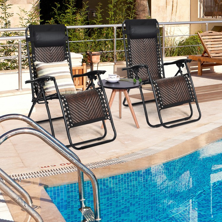 Two folding patio rattan zero gravity lounge chairs by the pool, featuring a durable steel frame and ergonomic design.