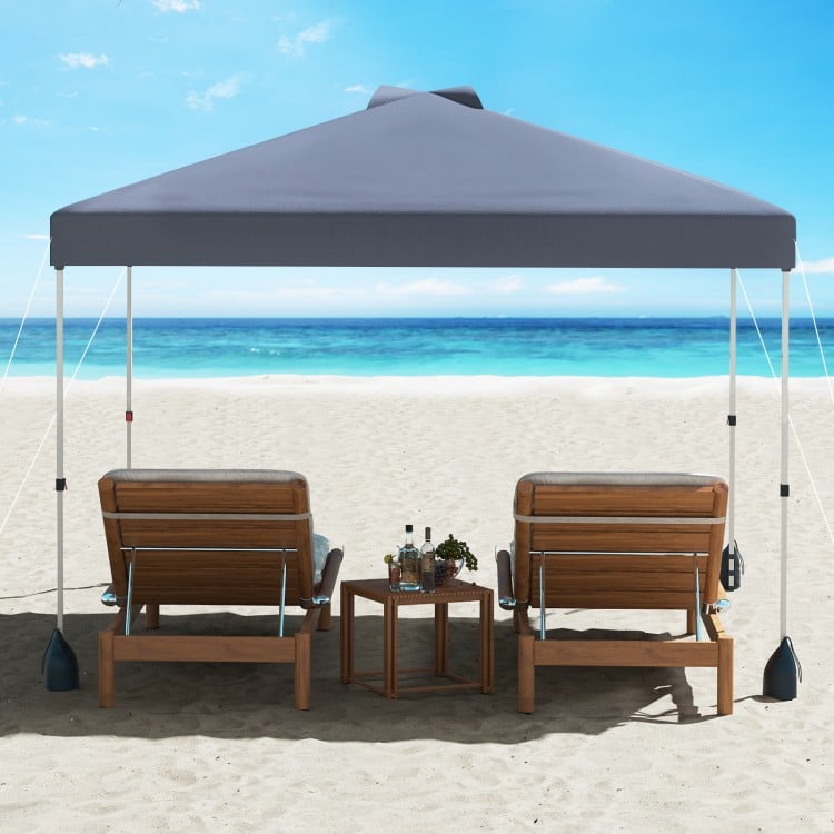 Gray 10 x 10 ft pop-up canopy tent with sidewall, set up on the beach with two lounge chairs and a small table.