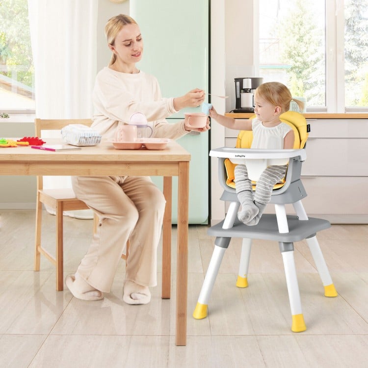 Convertible baby high chair in yellow with adjustable tray, used for feeding at the dining table.