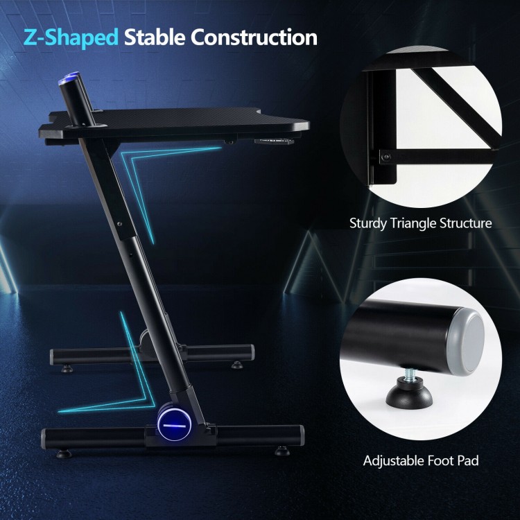 Z-shaped gaming desk with adjustable foot pads, carbon fiber surface, and blue LED lights for a stylish gaming setup.