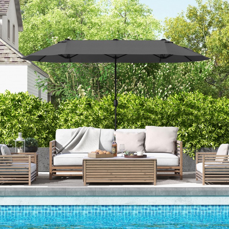 Double-sided gray patio umbrella with crank handle, providing ample shade for outdoor seating by the pool.