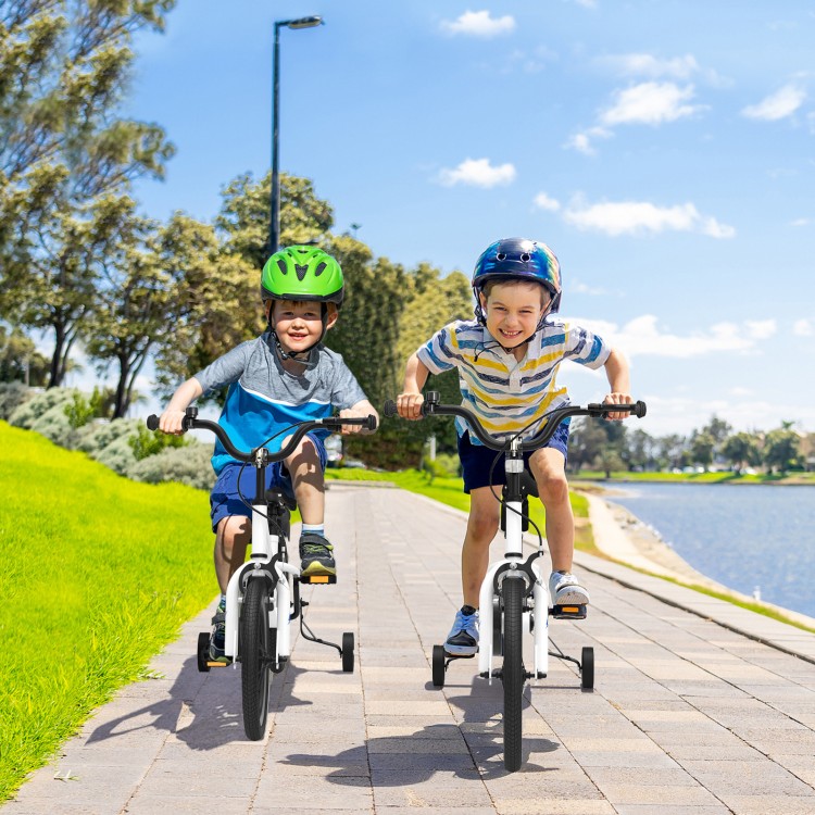 Two kids riding 16-inch white bikes with removable training wheels, enjoying outdoor fun by the water.