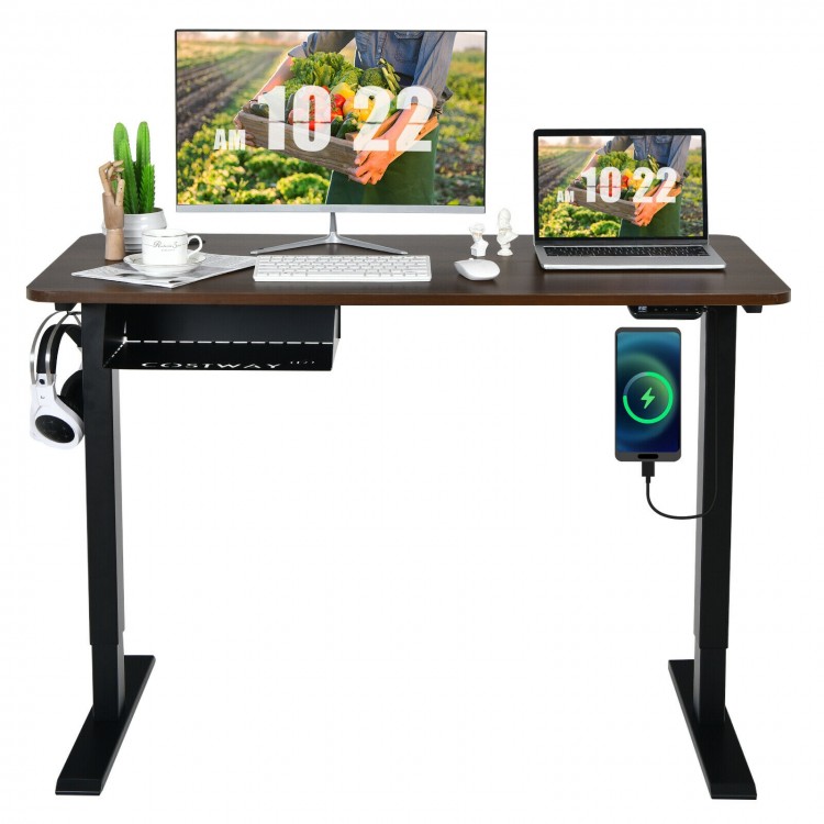 Electric height adjustable standing desk in walnut finish with dual monitors, USB charging port, and storage.
