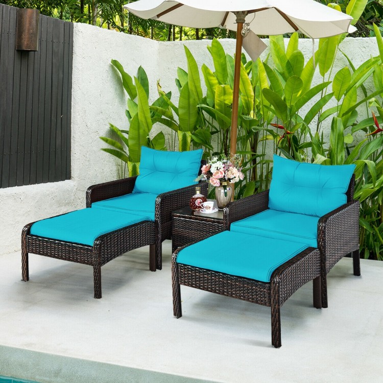 Two turquoise cushioned single sofas and ottomans in a brown rattan patio furniture set for outdoor relaxation.