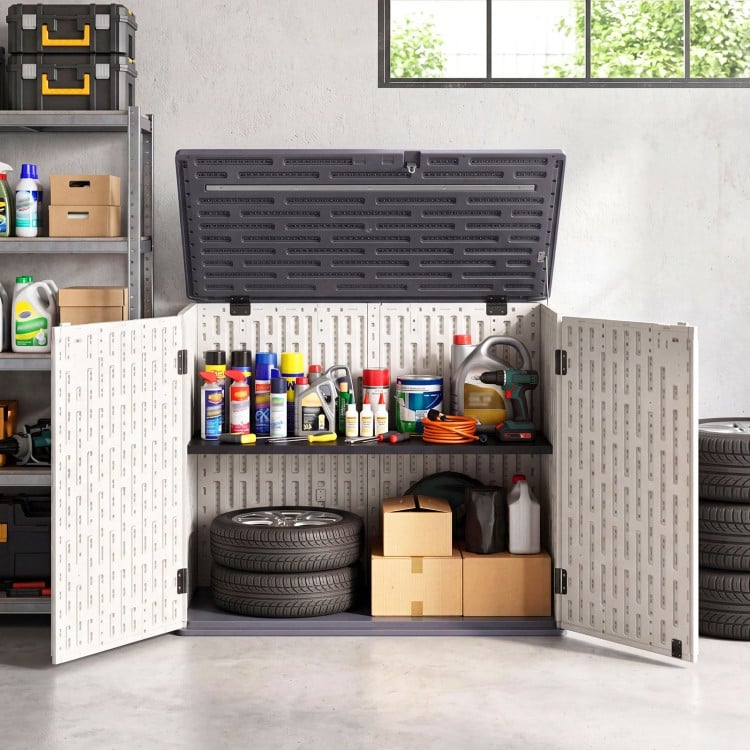 Horizontal resin storage shed with adjustable shelf, ideal for organizing garden tools and accessories in a garage.