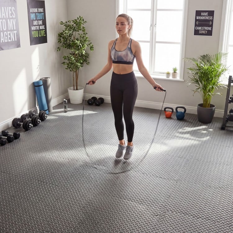 A woman jumps rope on 1/2" gray puzzle exercise floor mats, providing a non-slip, cushioned surface for workouts.