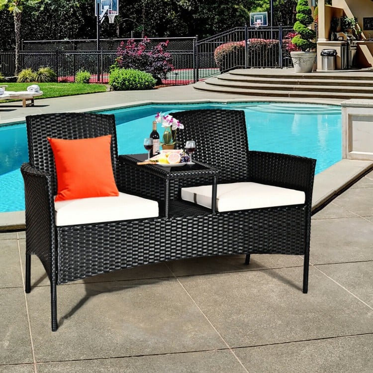 Wicker patio conversation set with removable cushions, featuring a tempered glass table, ideal for poolside relaxation.