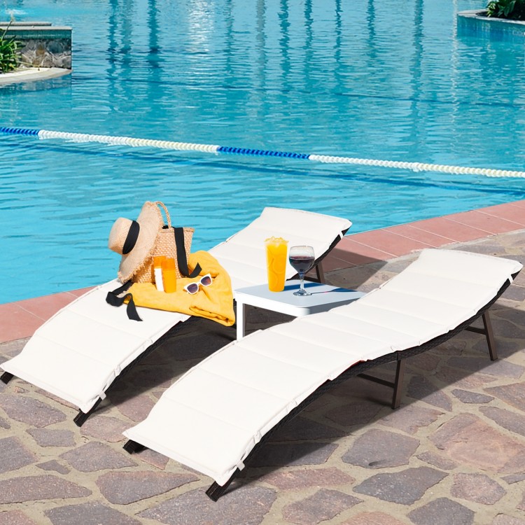 Folding patio lounger chairs in beige with a side table, perfect for poolside relaxation and sunbathing.