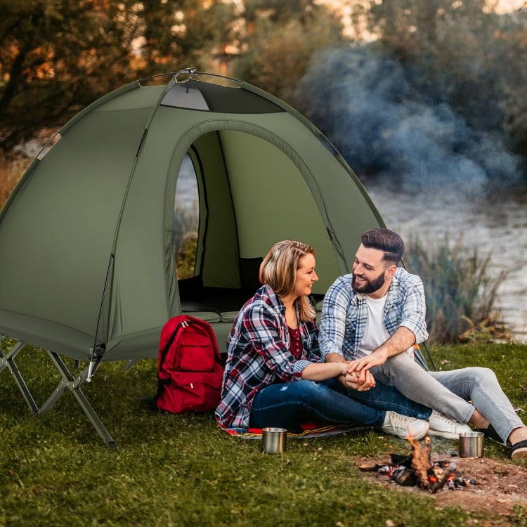 Couple enjoying a camping experience with a green 2-person cot tent, set up near a river for outdoor relaxation.