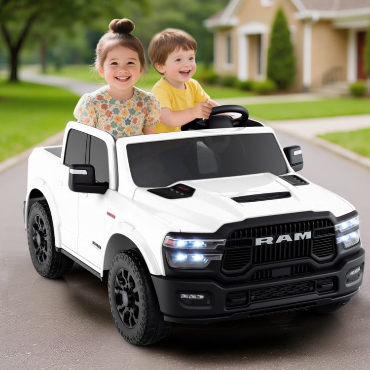 Two kids enjoying a ride in a white 2-seater licensed Ram truck toy with remote control and LED lights.