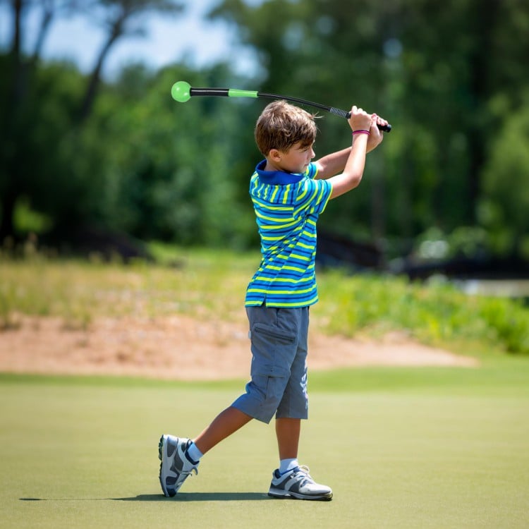 Child practicing golf swing with a 31.5-inch green swing trainer aid on a sunny course, enhancing grip and balance.