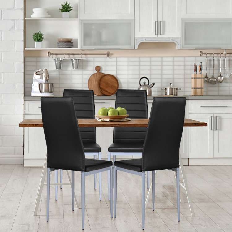 Four black PVC leather dining side chairs with painted steel legs around a wooden table in a modern kitchen setting.