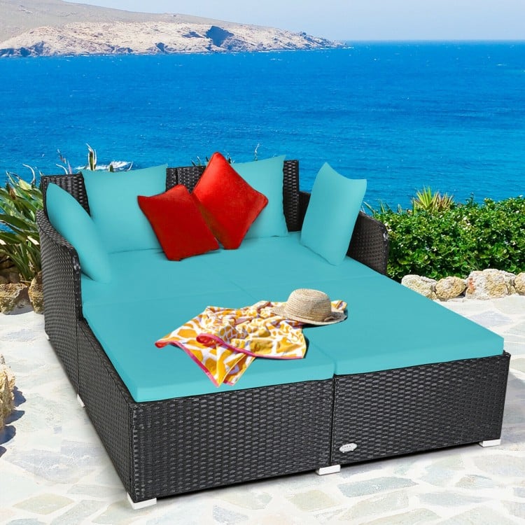 Spacious outdoor rattan daybed in turquoise with upholstered cushions and pillows, perfect for relaxation by the sea.