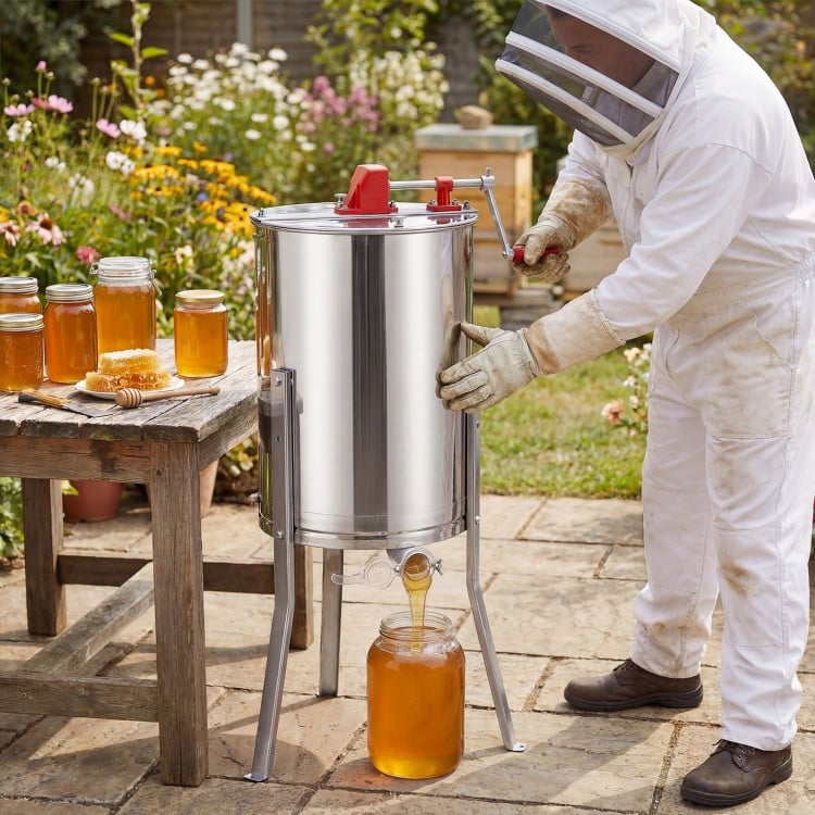 Manual honey extractor with clear lid, stainless steel construction, and adjustable height for home apiary use.