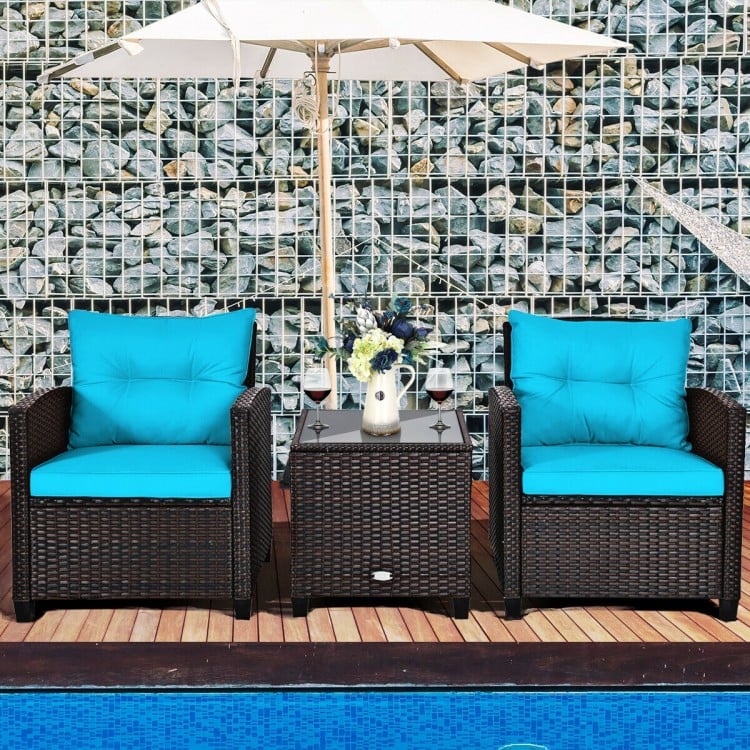 Two turquoise cushioned chairs and a coffee table in a rattan patio set, perfect for outdoor relaxation by the pool.