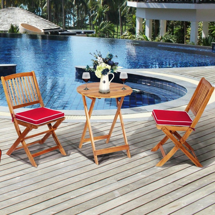 Folding wooden bistro set with red cushioned chairs and round table, perfect for outdoor relaxation by the pool.