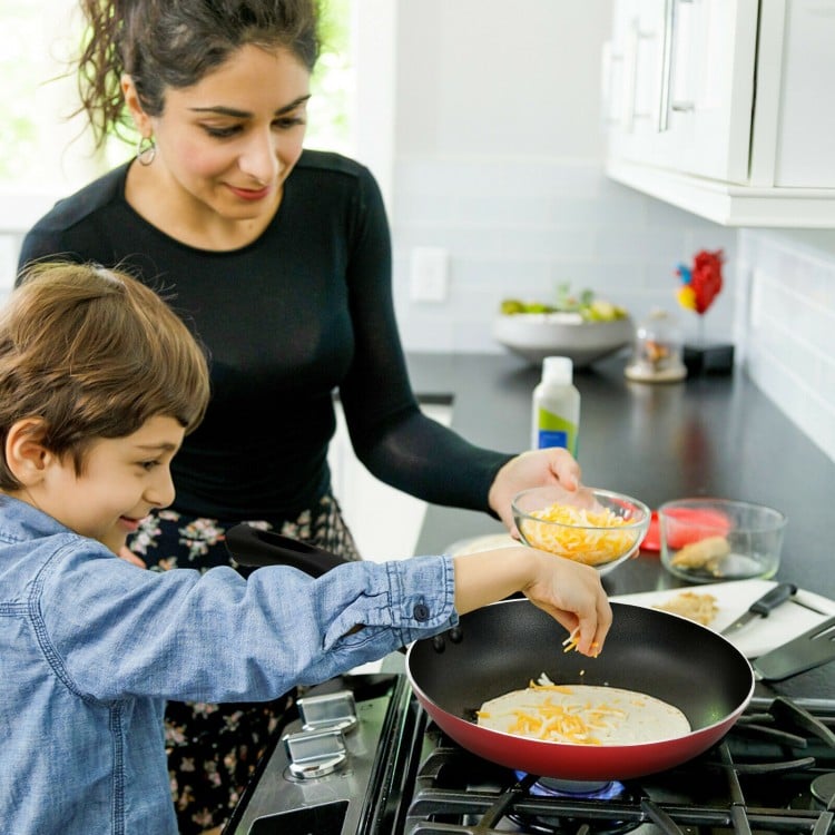 Child and adult cooking together with a nonstick frying pan from a 17-piece hard anodized cookware set.