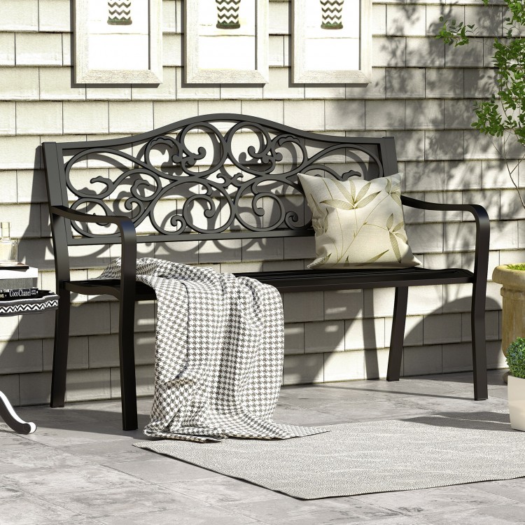 Black outdoor cast iron metal patio bench with floral design backrest, slatted seat, and cozy throw pillow for garden.