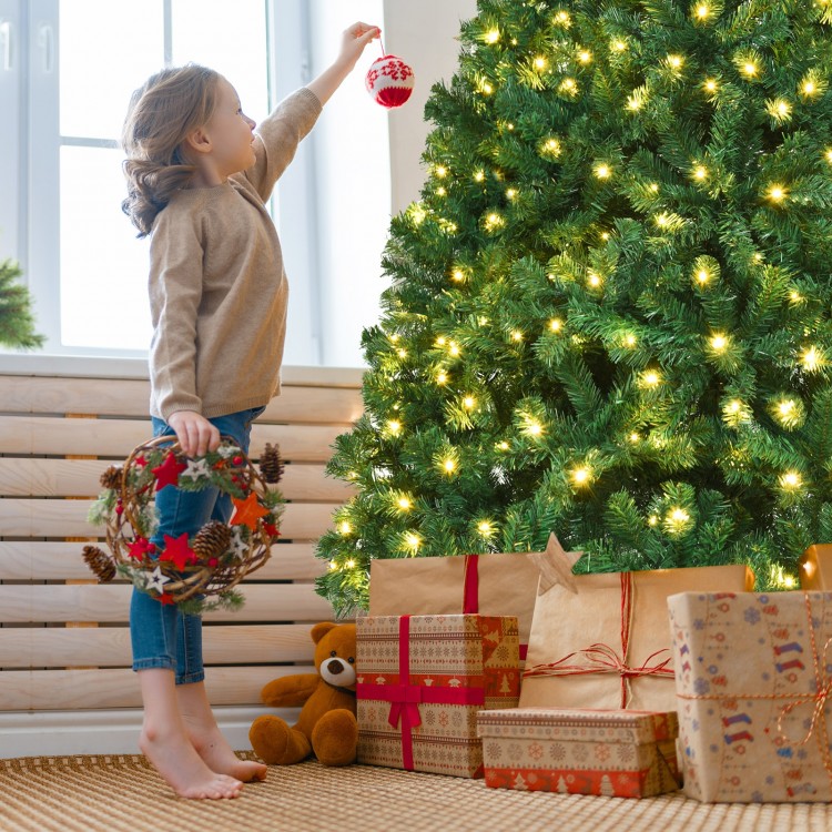 Child hanging a decoration on a 7-foot PVC artificial Christmas tree with LED lights, surrounded by wrapped gifts.