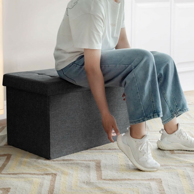 Foldable dark gray storage ottoman with padded seat, perfect for storing clothes and blankets in any room.