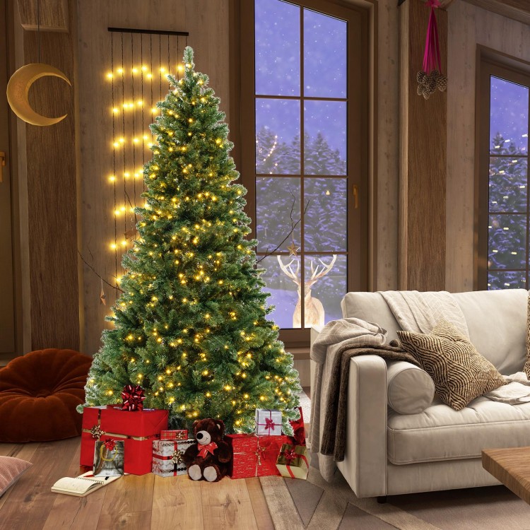 7 ft hinged Christmas tree with warm white LED lights and PVC branch tips, decorated with gifts in a cozy living room.