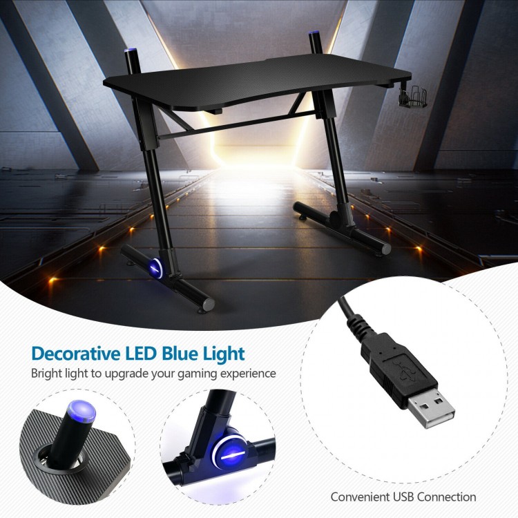 Height adjustable gaming desk with blue LED lights, carbon fiber texture, and sturdy Z-shaped legs for stability.