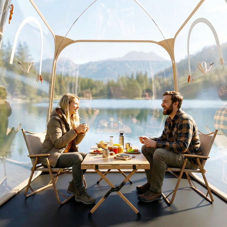 Clear bubble tent with two people enjoying a meal, showcasing the waterproof pod's spacious interior for outdoor.