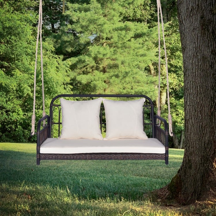 Wicker hanging porch swing with white cushions, designed for 2 people, suitable for outdoor use in gardens or backyards.