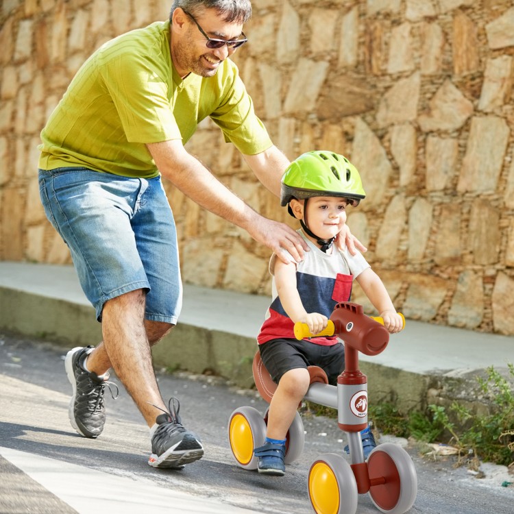 Child riding a brown baby balance bike with four wheels, featuring a cute horse head design, for safe outdoor fun.