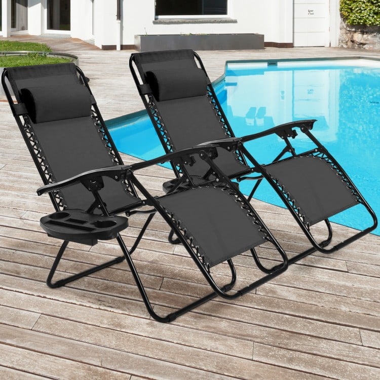 Two black folding lounge chairs with adjustable backs and cup holders, perfect for outdoor relaxation by the pool.