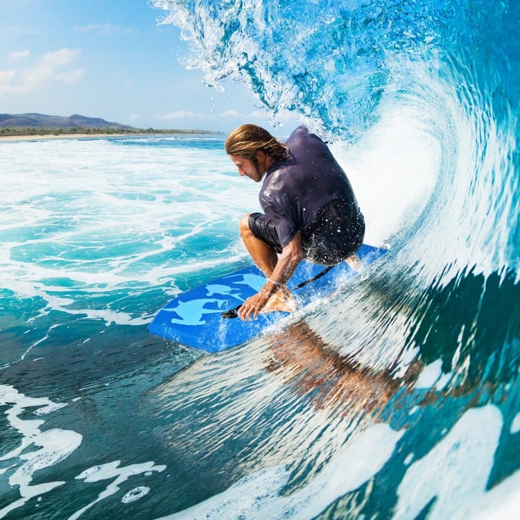 Surfer riding a wave on a blue Super Bodyboard with EPS core, designed for outdoor water sports and stability.