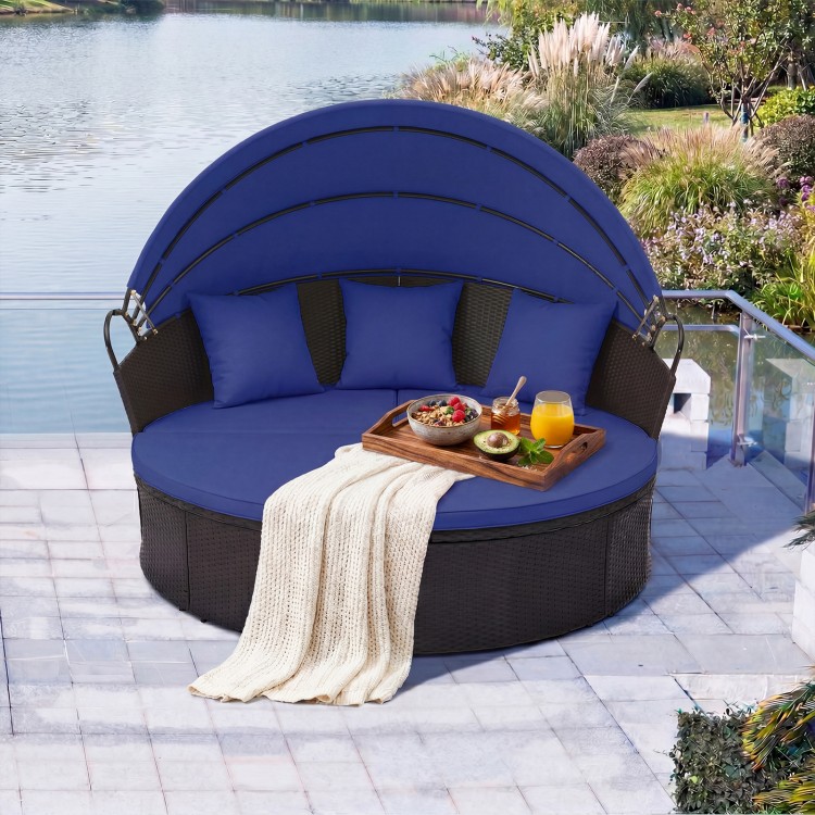 Round blue patio daybed with retractable canopy, wicker design, and pillows, perfect for outdoor relaxation by the.