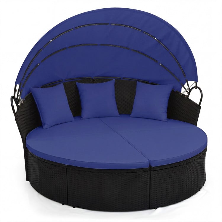 Round wicker patio daybed with retractable blue canopy and cushions, perfect for outdoor relaxation.