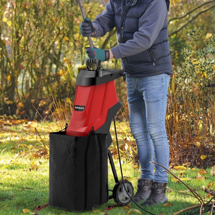 Electric wood chipper and shredder in red, shown in use for garden waste mulching with collection bag attached.