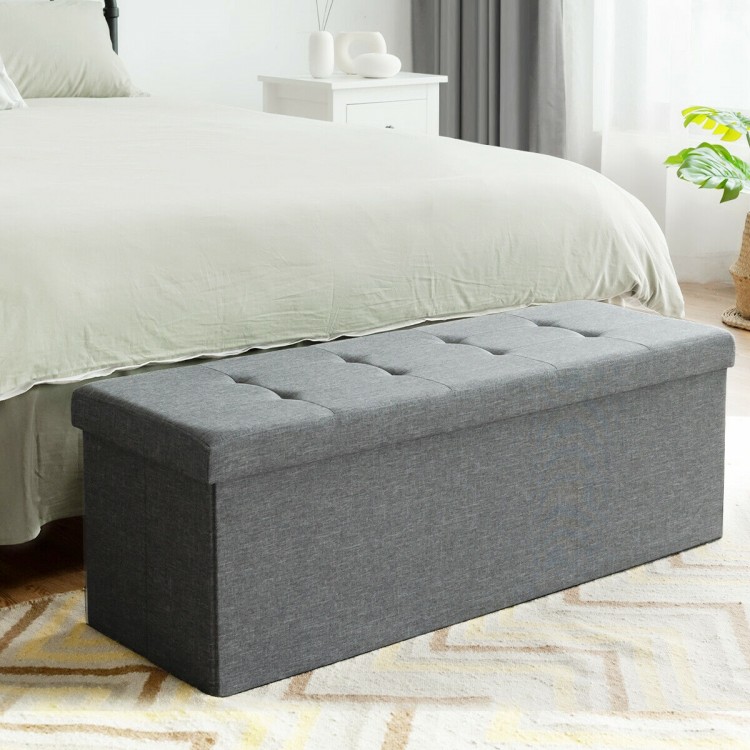 Light gray fabric folding storage ottoman with tufted design, ideal for storing blankets and shoes at the bed end.
