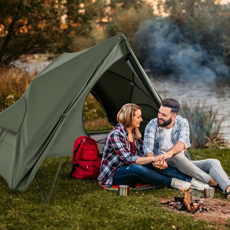Foldable 2-person camping cot tent in green, set up by a lake, ideal for camping and outdoor adventures.