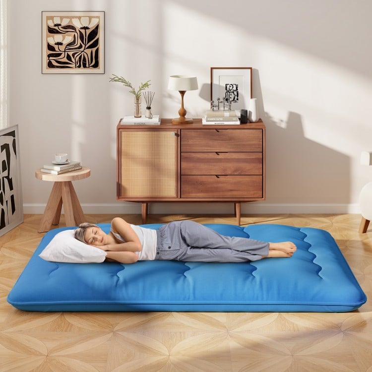 Blue foldable futon mattress with washable cover, shown in a living room setting, ideal for camping and home use.