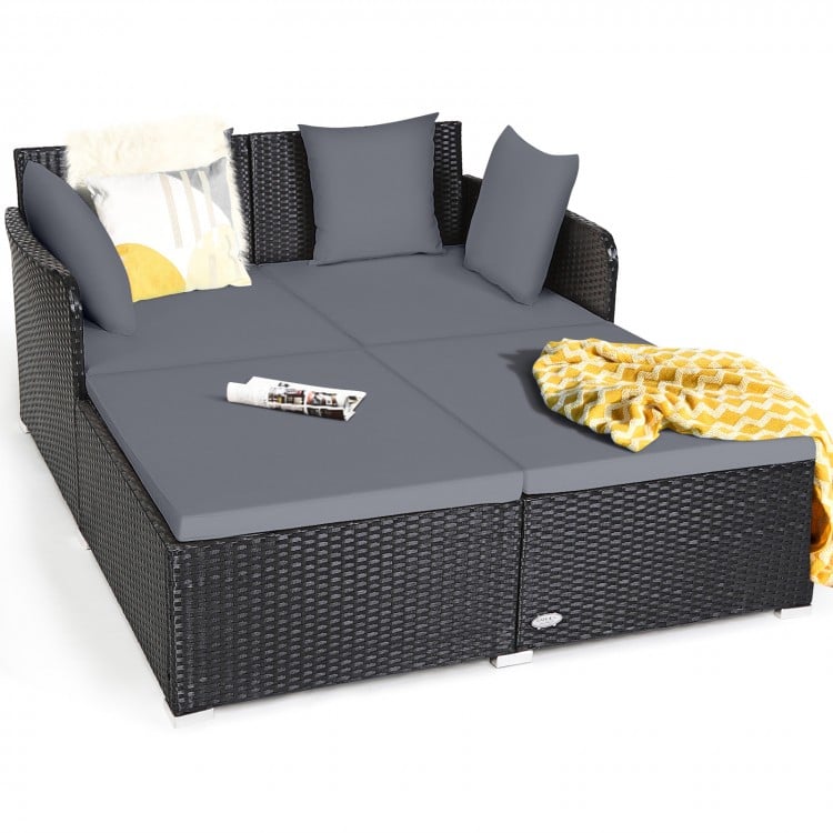 Spacious outdoor rattan daybed with gray upholstered cushions, featuring armrests and a curved backrest for comfort.