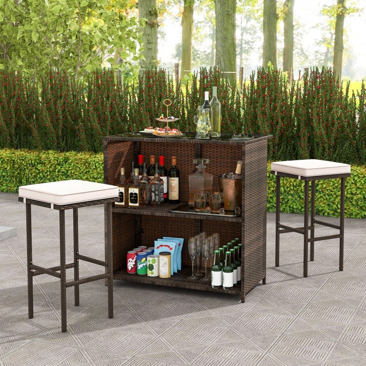 Rattan patio bar set with tempered glass tabletop and cushioned stools, perfect for indoor and outdoor gatherings.