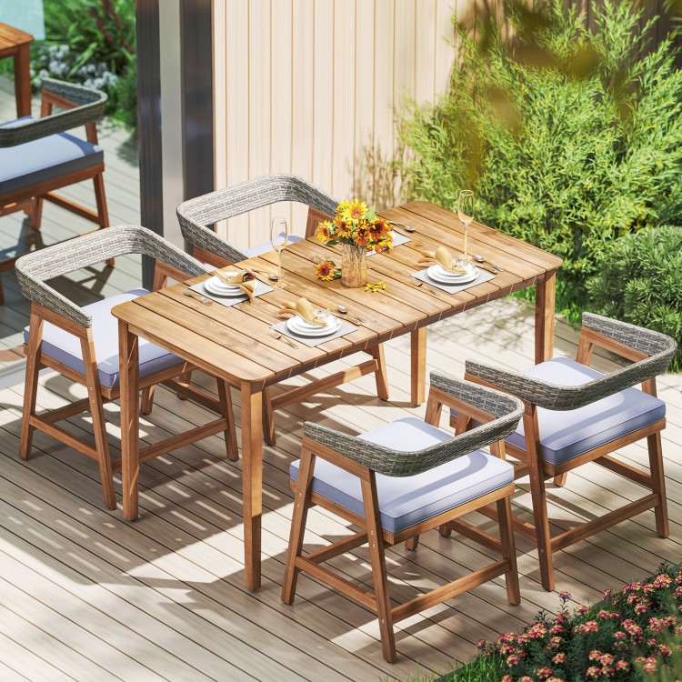 Outdoor acacia wood dining set with four gray wicker chairs and cushions, perfect for backyard or patio dining.
