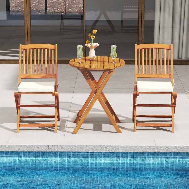 Two outdoor folding chairs with beige seat cushions and a round acacia wood table, perfect for poolside dining.