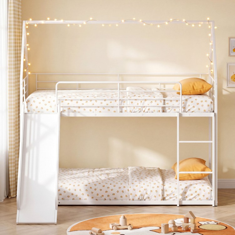House-shaped metal twin over twin low bunk bed in white with slide, safety guardrails, and decorative fairy lights.