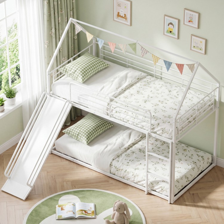House-shaped metal twin over twin low bunk bed in white with slide, safety guardrails, and decorative details for kids.