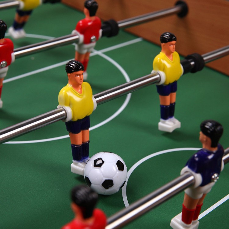 Foosball game table featuring yellow and red player figurines with a soccer ball on a green playing surface.