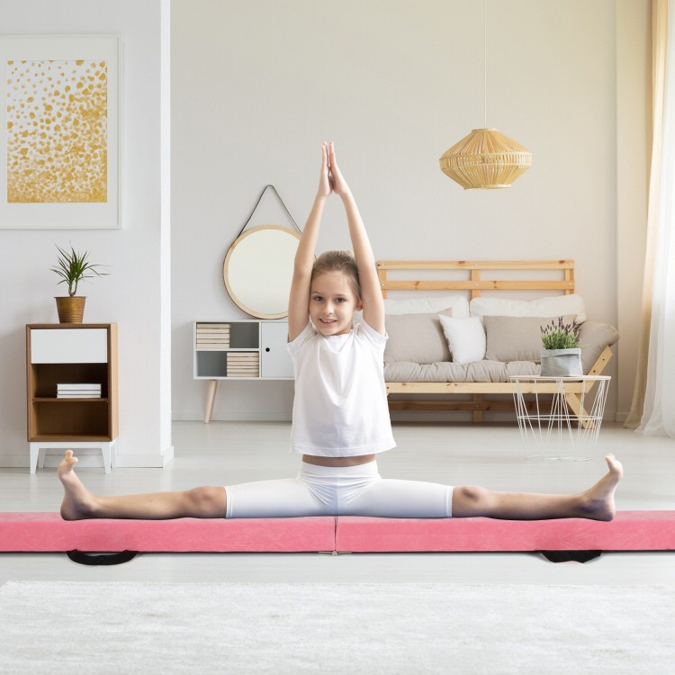 Child performing a split on a pink 9 FT folding gymnastics balance beam with a pine wood frame in a bright living room.