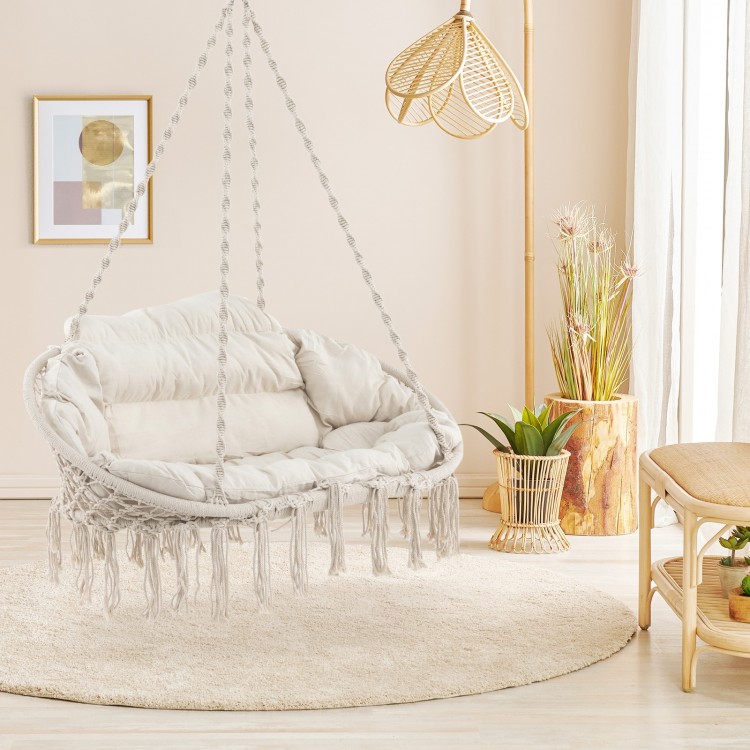 Hand-woven rope hanging chair in beige with thick cushion, featuring elegant tassels for bohemian decor and comfort.