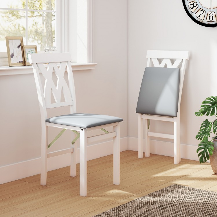 White folding wooden dining chairs with faux leather upholstery, featuring X-shaped backrests, ideal for small spaces.