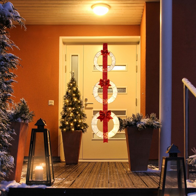 Set of 3 lighted Christmas wreaths with warm white LEDs and bows, hanging elegantly on a doorway for festive decor.