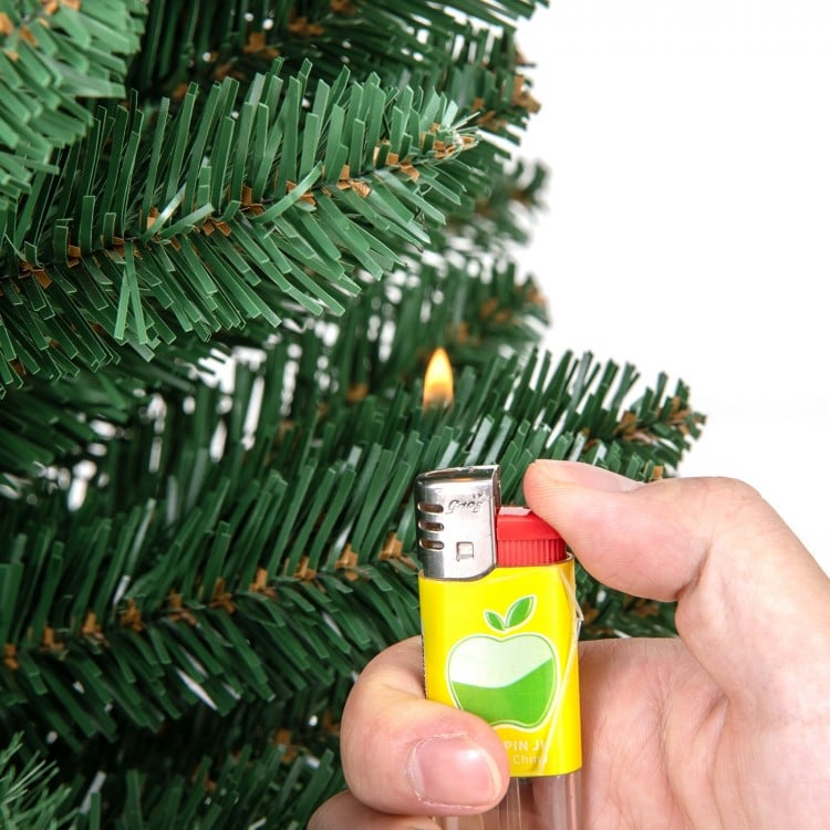 Hand holding a lighter igniting a branch of a Pencil Christmas Tree with warm LED lights and memory wire tips.