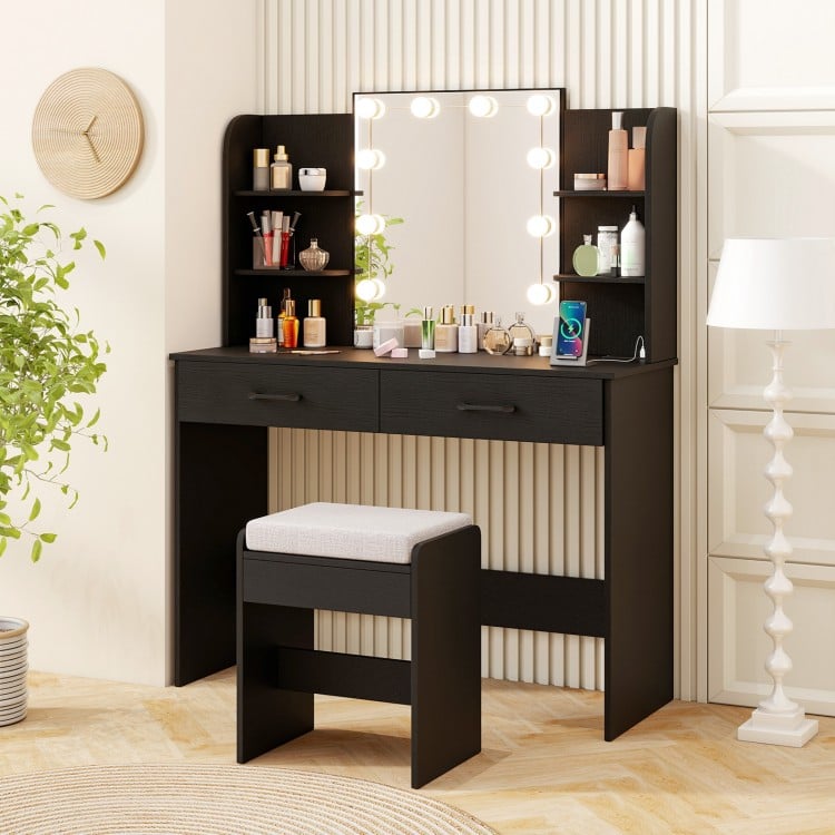 Vanity set in black featuring a lighted mirror, cushioned stool, and ample storage with drawers and shelves for beauty.